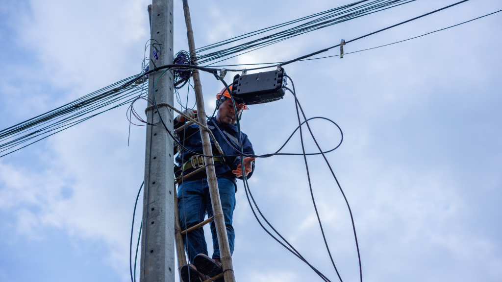 Telecoms engineer servicing a telephone pole up a ladder, representing a temporary job site.